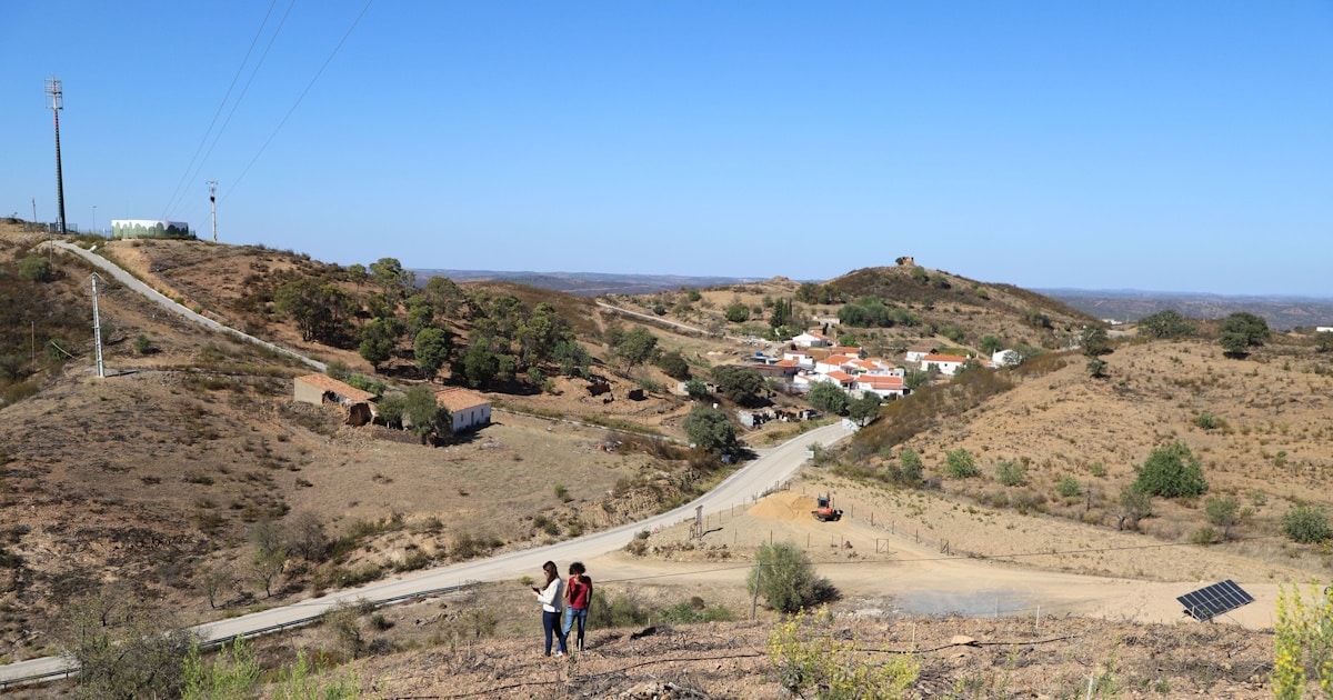 Paisagem rural, pessoas caminhando, aldeia portuguesa ao fundo.