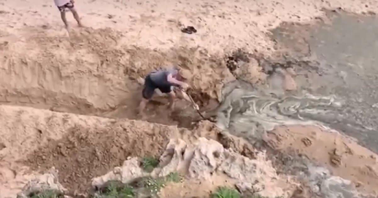 Pessoa escavando na areia com água corrente.