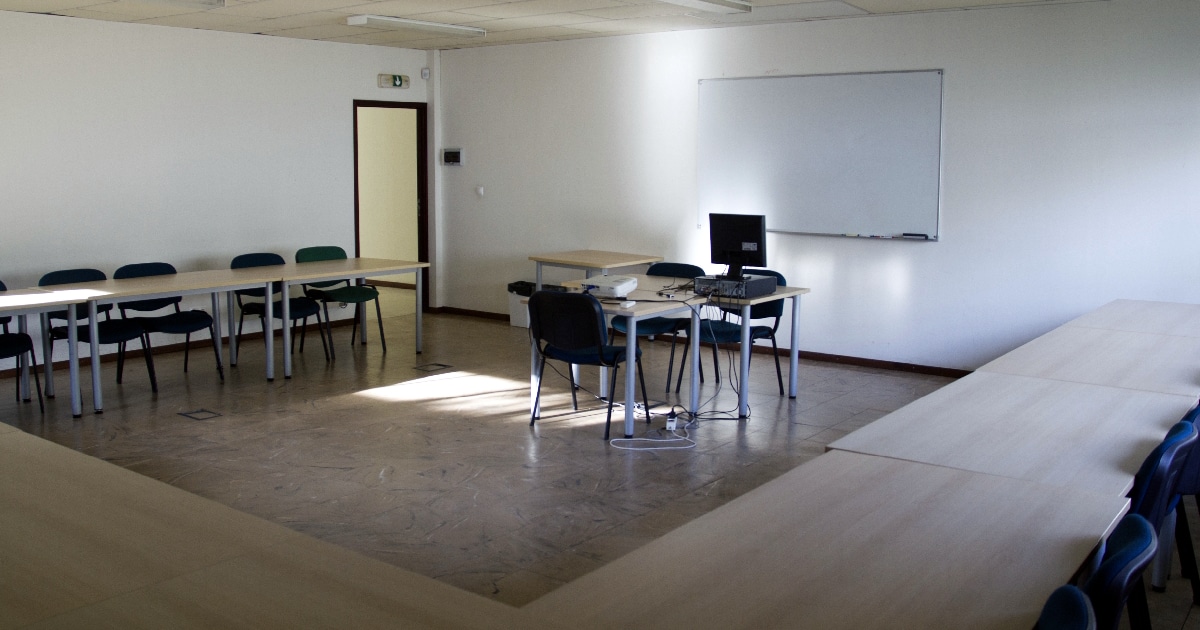 Sala de aula vazia com quadro branco e computador.
