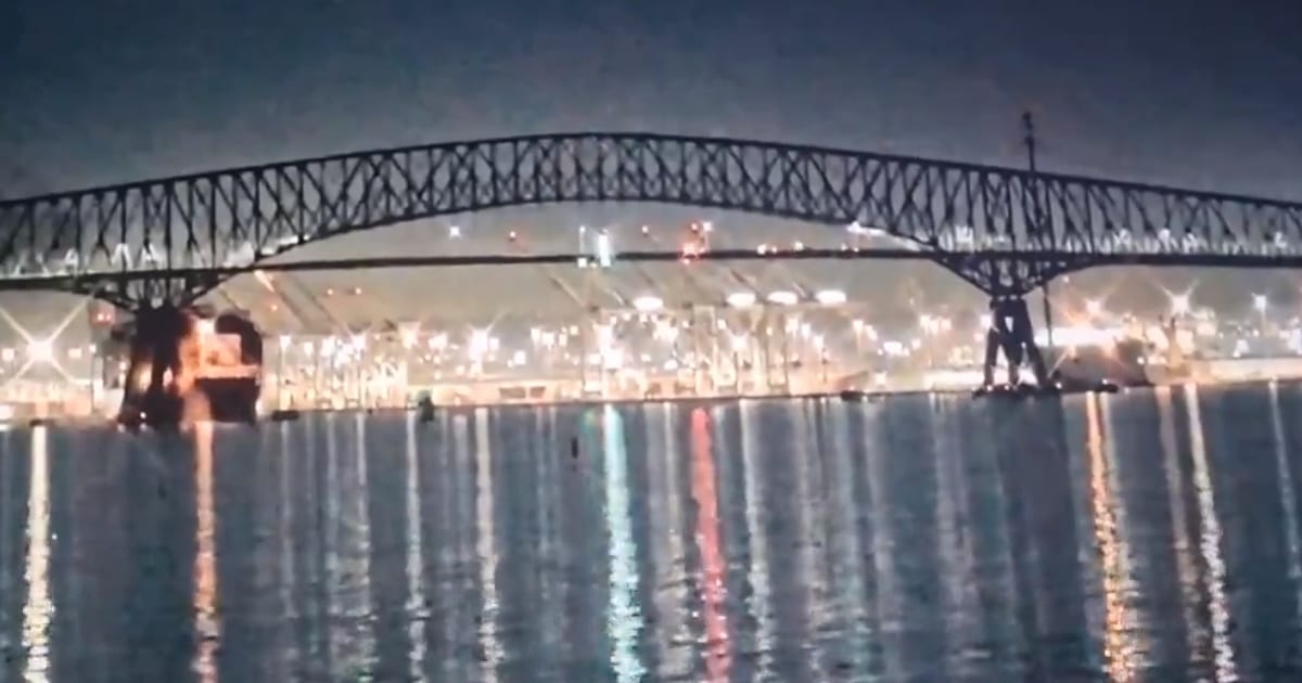 Ponte metálica iluminada sobre rio à noite.