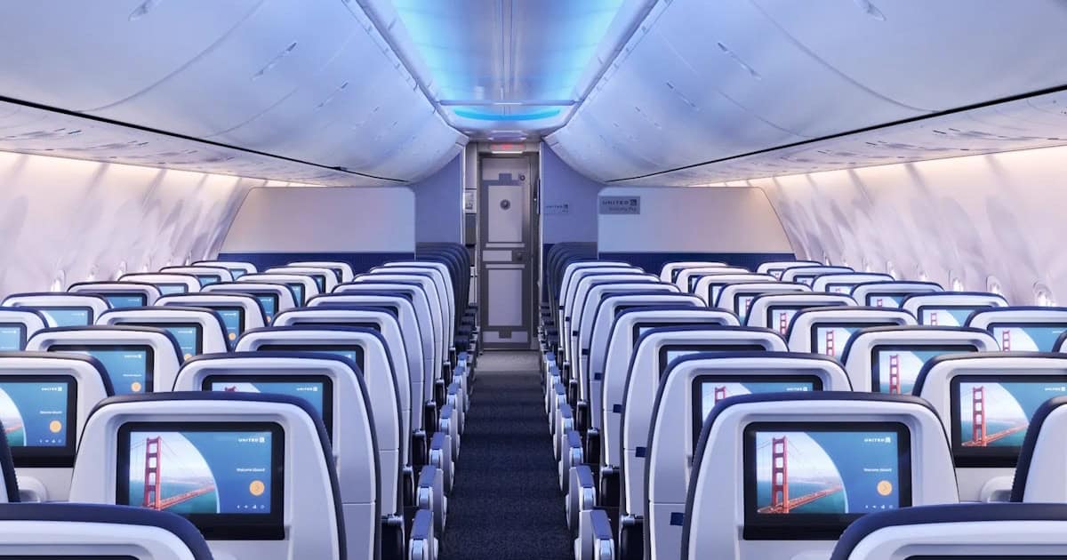 Interior de avião com assentos e ecrãs.